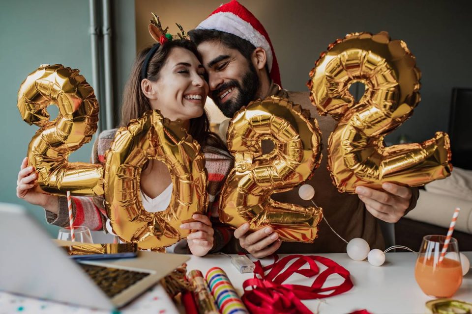 Casal abraçado segurando balões que remetem ao ano de 2022