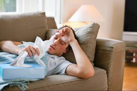 Na imagem colorida, um homem está deitado em uma cama com as mãos na cabeça