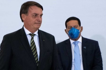 Na imagem colorida, dois homens estão posicionados no centro. Eles usam terno e gravata na cor preta e camiseta branca. Eles tem cabelos curtos e escuros