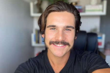 Foto colorida do ator Nicolas Prattes sorrindo e usando uma blusa preta