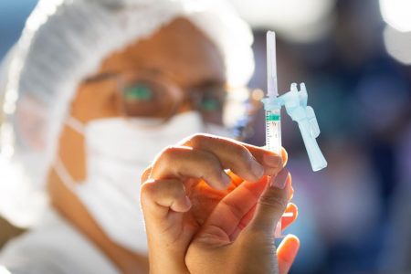 Mulher de óculos e máscara mostrando agulha com vacina