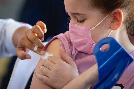 Menina de máscara rosa aperta algodão contra o braço