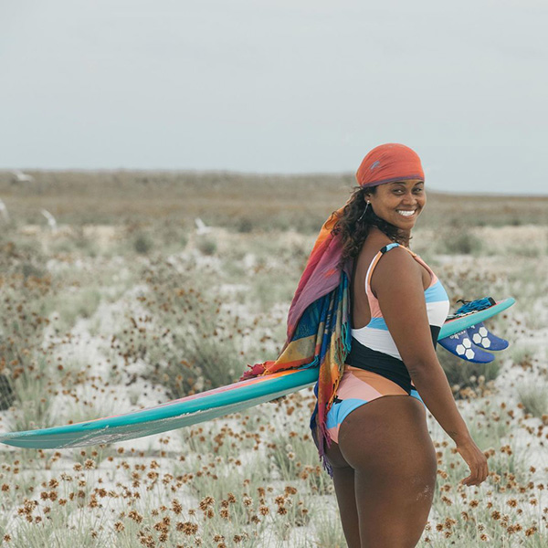 Mulher negra em praia e com prancha de surfe