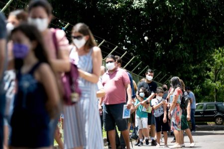 Fila de adultos e crianças com máscara