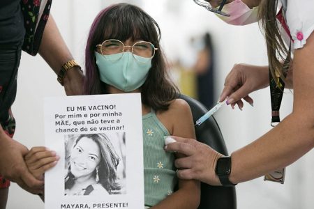 Helena - Criança de 8 anos se vacina e segura foto da mãe morta pela Covid