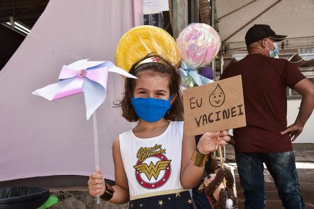 Menina com roupa da mulher maravilha segurando cata-vento e placa