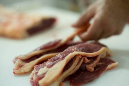 Imagem colorida mostra peças de picanha fatiadas com a mão de um homem ao fundo. A carne vermelha está em pedaços - Metrópoles
