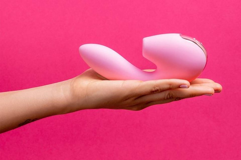 Mão feminina segurando um vibrador rosa em um fundo rosa mais escuro