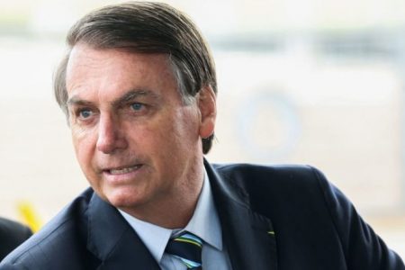 Bolsonaro cumprimenta turistas na frente do Alvorada. Ele usa terno e gravata e olha para o lado - Metrópoles