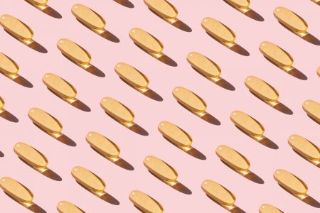 cápsulas de vitamina D em fundo rosa