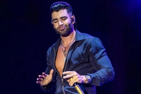 Gusttavo Lima cantor sertanejo em show. Ele tem cabelos pretos, barba preta e usa camisa preta