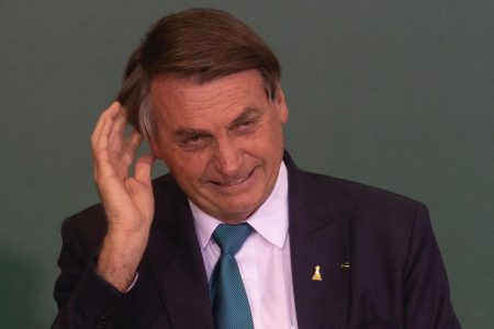 Em evento no Planalto do projeto "Brasil para Todos", Bolsonaro sorri enquanto olha de baixo e coça a cabeça. Ele usa terno e está sem máscara - Metrópoles
