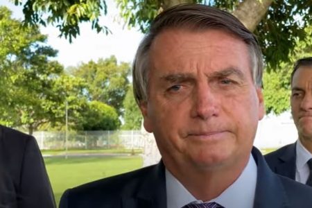 O presidente Bolsonaro conversa com apoiadores no cercadinho do Alovorada. Ele está sem máscara, sério, e rodeado por pessoas - Metrópoles