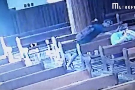 Foto: Homem de camisa preta e boné pegando uma bolsa de outra pessoa em uma igreja.