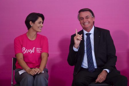 Michelle e Jair Bolsonaro em cerimônia de comemoração do Dia da Mulher no Palácio do Planalto. Eles sorriem um para o outro - Metrópoles