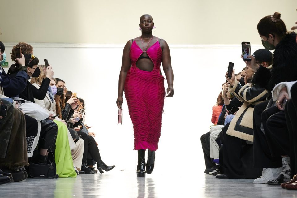 Mulher negra e careca desfilando. Ela usa um vestido franzido rosa da marca Ester Manas