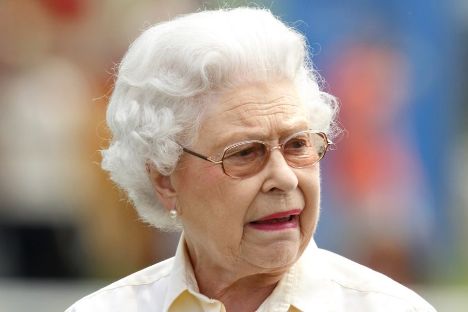 Foto colorida. Rainha Elizabeth faz careta. Ela veste uma blusa branca