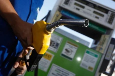 Pessoa segurando bico de abastecimento em frente a uma bomba de gasolina