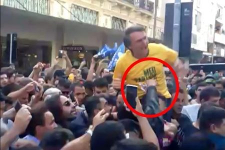 Foto colorida do momento em que o presidente Bolsonaro, então candidato, é vítima de atentado à faca em Juiz de Fora, Minas Gerais. Ele está no meio de uma multidão e o cirminoso enfia uma faca em sua barriga - Metrópoles