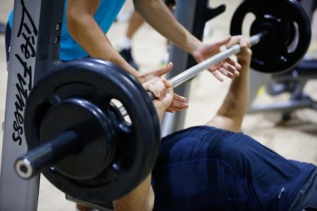 Foto colorida de pessoa fazendo um exercício com a ajuda de outra