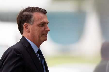 Presidente Bolsonaro fala de perfil do lado de fora do palácio da Alvorada, no cercadinho onde ficam seus apoiadores e jornalistas. Ele usa terno - Metrópoles
