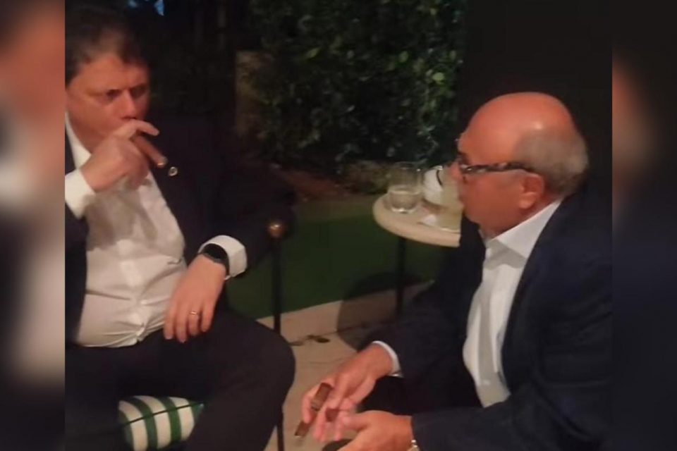 O ministro da Infraestrutura, Tarcísio de Freitas, fuma um charuto ao lado do empresário Washington Cinel, da Gocil - Metrópoles