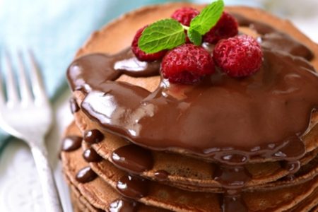 Panqueca de chocolate com calda de chocolate e frutas vermelhas por cima, decoradas com ramo de hortelã - Metrópoles