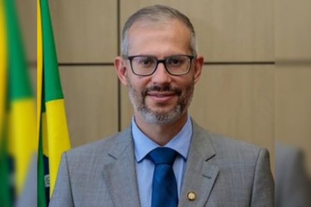 Victor Godoy Veiga, até então secretário-executivo do Ministério da Educação, foi nomeado ministro interino da pasta após a saída de Milton Ribeiro. Na foto ele sorri, frente à bandeira do Brasil numa sala, e usa terno - Metrópoles