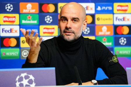 Pep Guardiola, treinador do Manchester Ciry, fala à imprensa em entrevista antes de jogo da Champions League, diante de painel de patrocinadores - Metrópoles