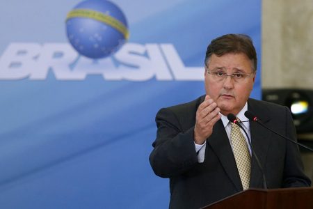Geddel Vieira usa terno preto enquanto discursa em palanque. Atrás há um mural com a logo do governo federal - Metrópoles