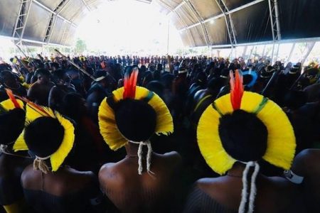 Foto colorida de dois indígenas em frente ao acampamento