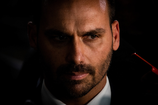 O deputado federal Eduardo Bolsonaro de frente, com parte do rosto na penumbra, olha para o lado com - Metrópoles