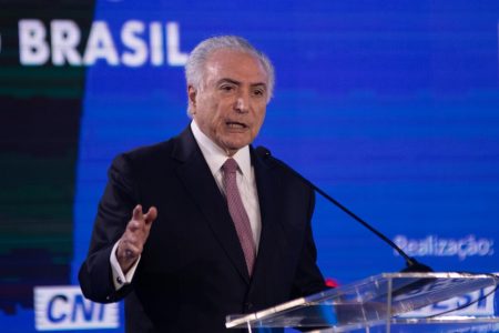 Ex-presidente da República, Michel Temer fala durante evento da CNI. Ele usa terno e está diante de telão azul frente a pulpito com microfone - Metrópoles