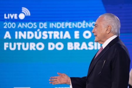 Ex-presidente da República, Michel Temer fala durante evento da CNI. Ele usa terno e está diante de telão azul frente a pulpito com microfone - Metrópoles