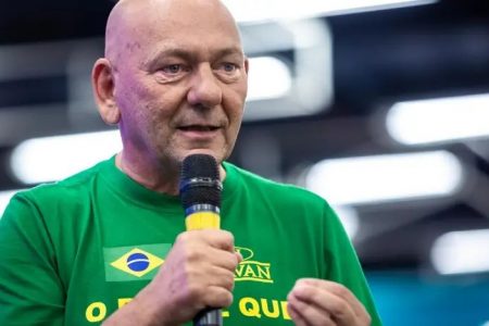 O empresário brasileiro e dono da loja Havan, Luciana Hang, fala em evento com microfone na mão. Ele usa camisa da empresa com as cores verde e amarela - Metrópoles