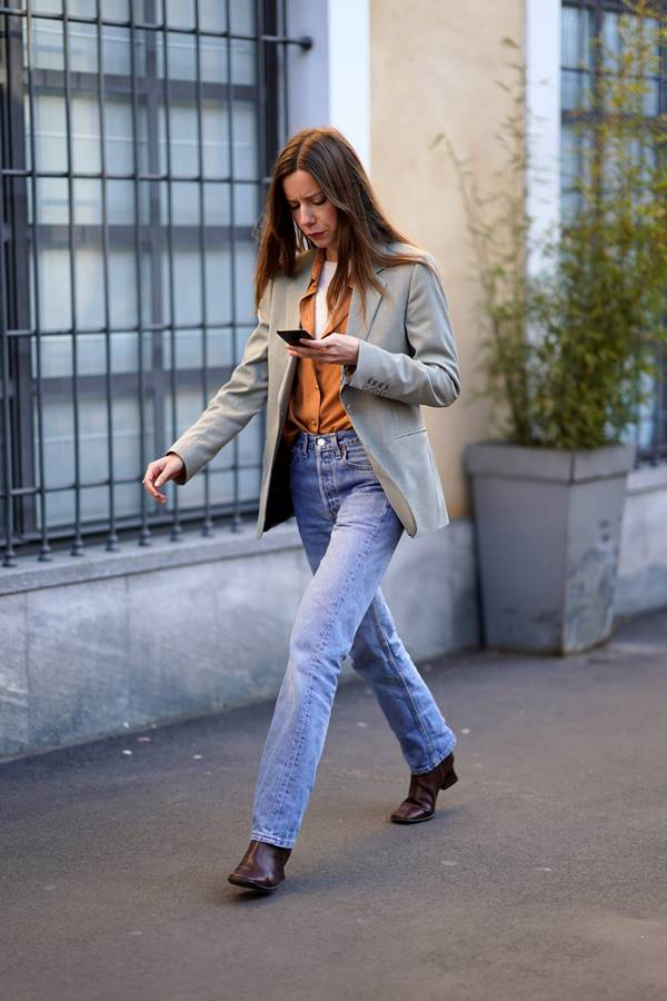 Mulher branca andando na rua com calça jeans e blazer claro