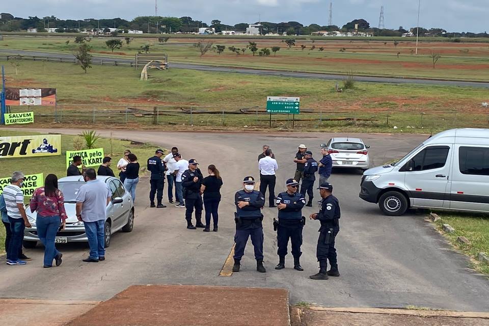 Policiais militares cumprem ordem da justiça e impedem demolição do kartódromo de Brasília, próximo ao Aeroporto Iternacional. Na foto, pessoas conversam policiais próximos a cartazes - Metrópoles