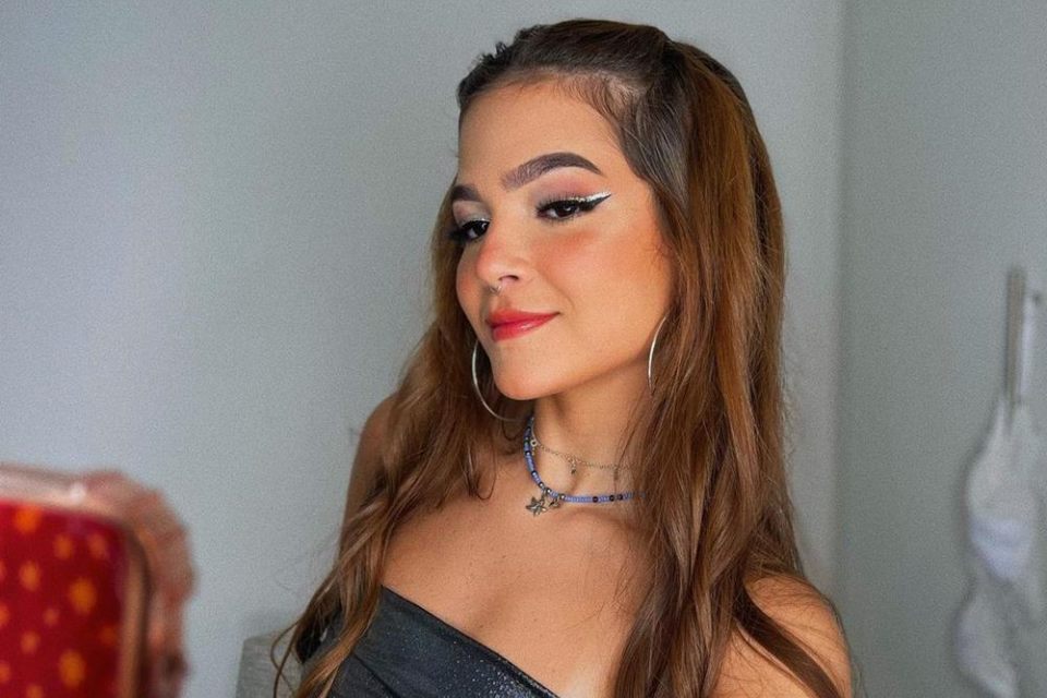 A atriz Mel Maia. Ela tem cabelo castanho longo, usa um colar e brincos, delineador branco e um cropped preto - Metrópoles