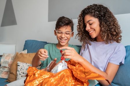 duas crianças abrem um ovo de páscoa. a menina aparenta ser mais velha que o garoto