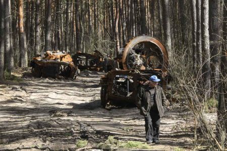 Homem passa perto de máquinas militares russas destruídas na floresta no norte de Kiev, Ucrânia