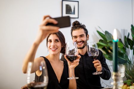 casal segurando celular e garrafa de vinho