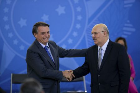 Jair Bolsonaro e Milton Ribeiro se cumprimentam com um aperto de mãos. Os dois usam terno e sorriem