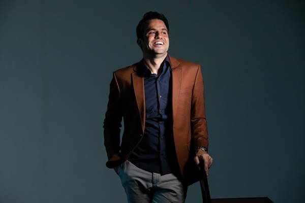 Fotografia colorida de homem em pé com mão sobre cadeira