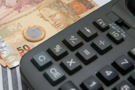 Cédulas e moedas ao lado de uma calculadora preta - Metrópoles