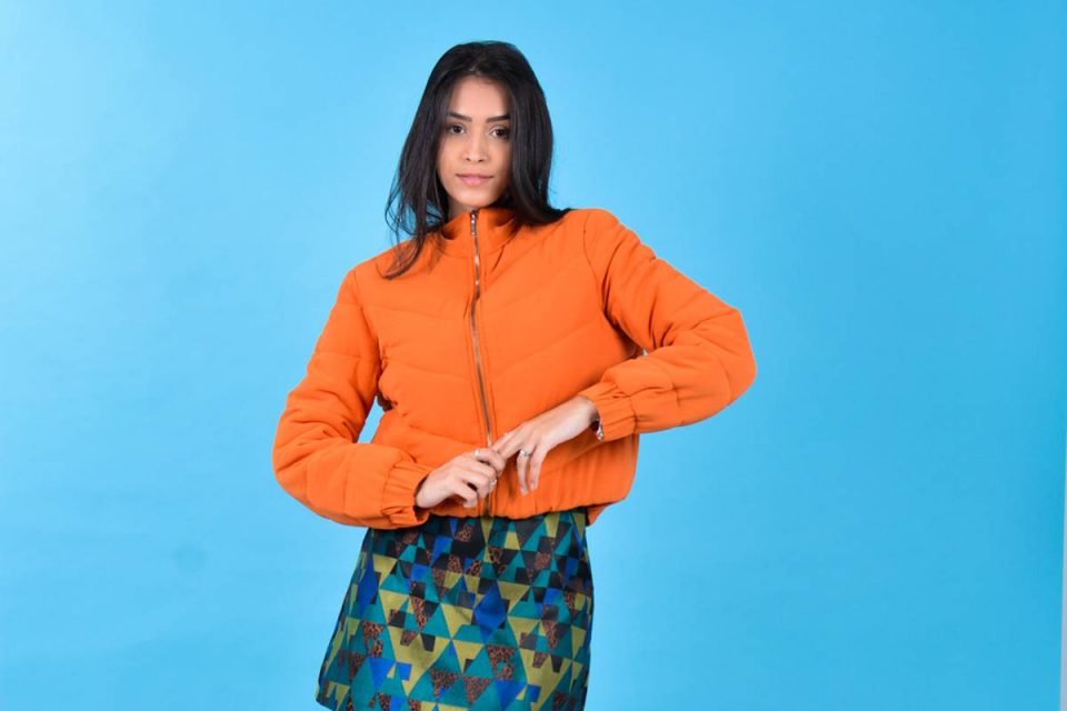 Modelo branca com cabelos longos usa saia com estampas geométricas, bota de cano alto preta e jaqueta acolchoada