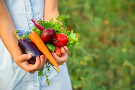 Imagem colorida de criança segurando vegetais nas mãos em fundo verde - Metrópoles