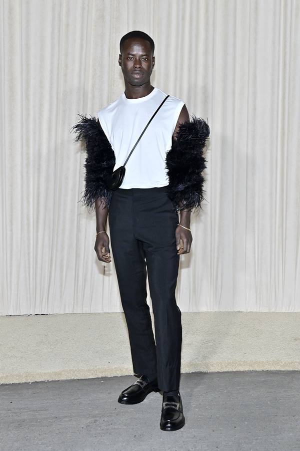 Homem negro usando blusa branca com detalhe de plumas nas mangas