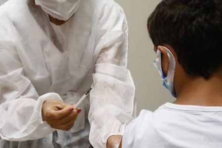 Fotografia colorida de profissional de saúde mostrando seringa para criança