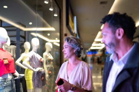 homem e mulher brancos olham a vitrine de uma loja dentro de um shopping