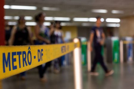 Movimentação desfocada no metrô do DF, estação Praça do Relógio, em Taguatinga. Em primeiro plano, a faixa de contenção amarela e azul escrito "METRÔ-DF" - Metrópoles